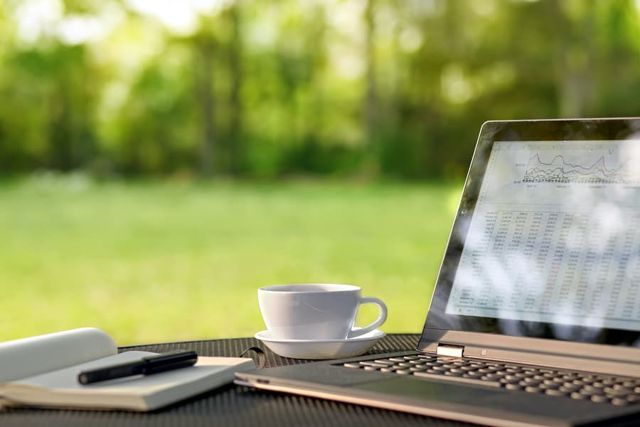 A photo of a laptop, paper notebook, and cup of coffee sitting on a table outside.