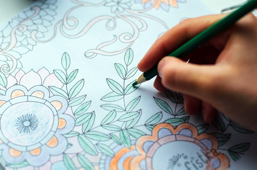 A photo of a person coloring a picture of flowers with colored pencils.