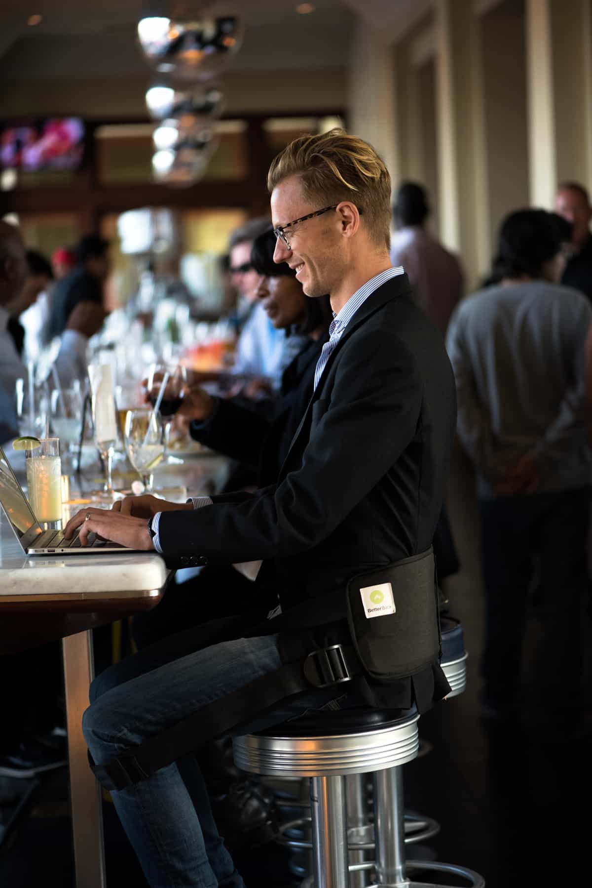 A photo of a man wearing the BetterBack while sitting on a stool.