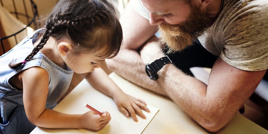 A photo of a father and daughter sitting down to draw.