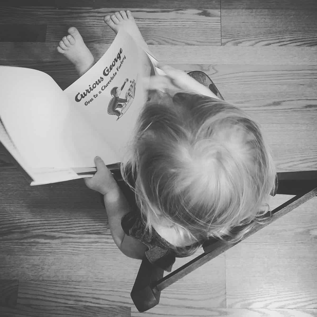 A photo of a child reading a Curious George book.