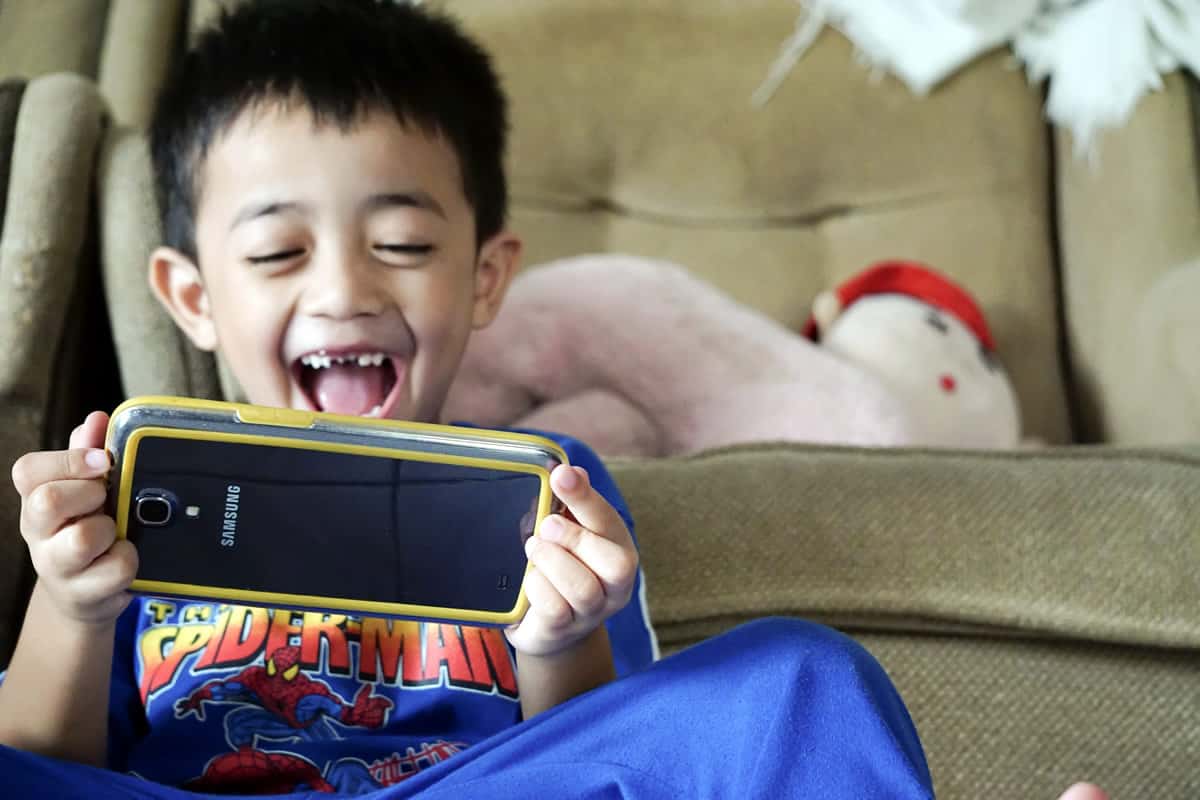 A photo of a happy child playing a game on a smartphone.