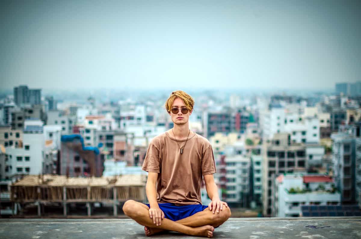 Image of a man meditating on top of building with a city surrounding him.