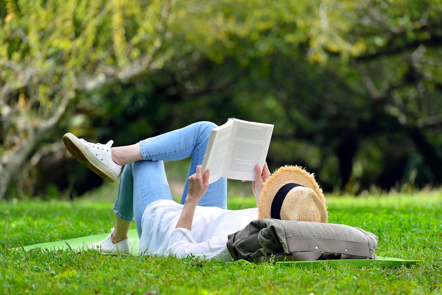 A photo of a woman lying in the grass and reading a book on a beautiful summer day.