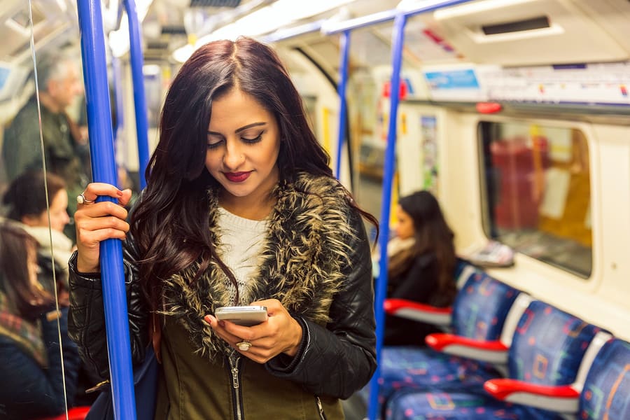 A photo of a woman looking at her smartphone while standing on the subway.