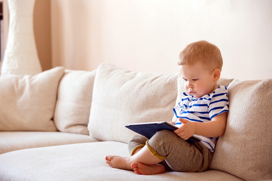 A photo of a child playing with a tablet on a couch.