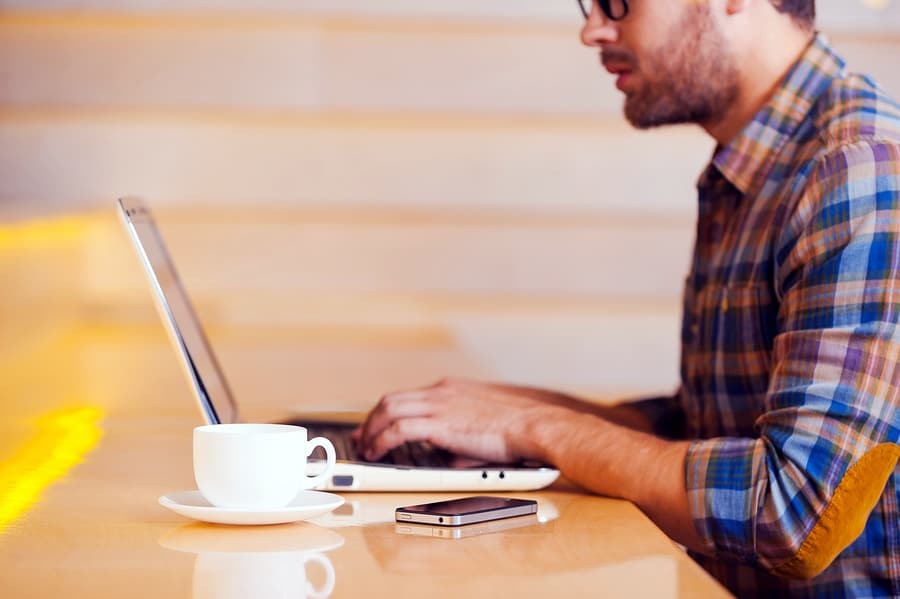 A photo of a man working on his laptop in a coffee house.