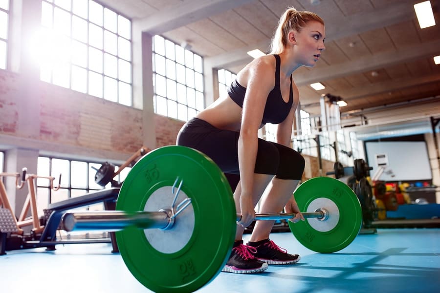 A photo of a woman preparing to do a deadlift with a large barbell and extra weights.