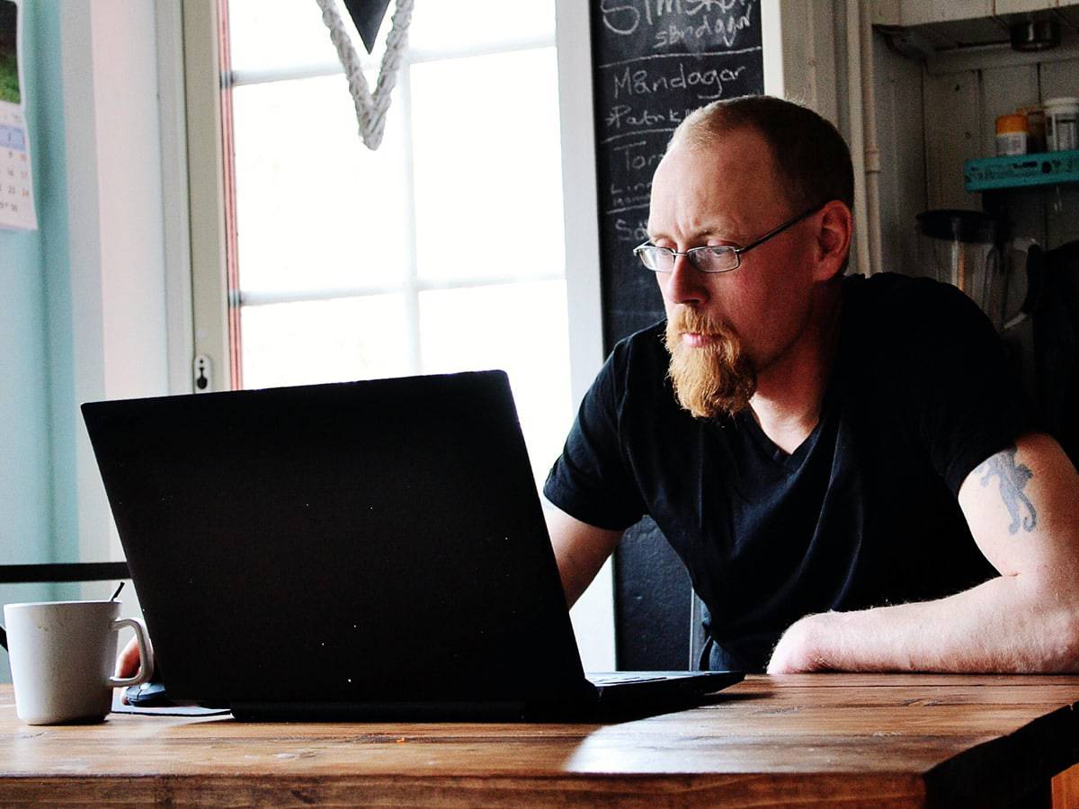 A photo of a man working at his kitchen table with a fresh mug of coffee.