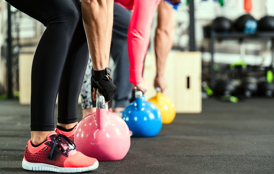 A photo of three people preparing for an exercise using heavy kettlebells.