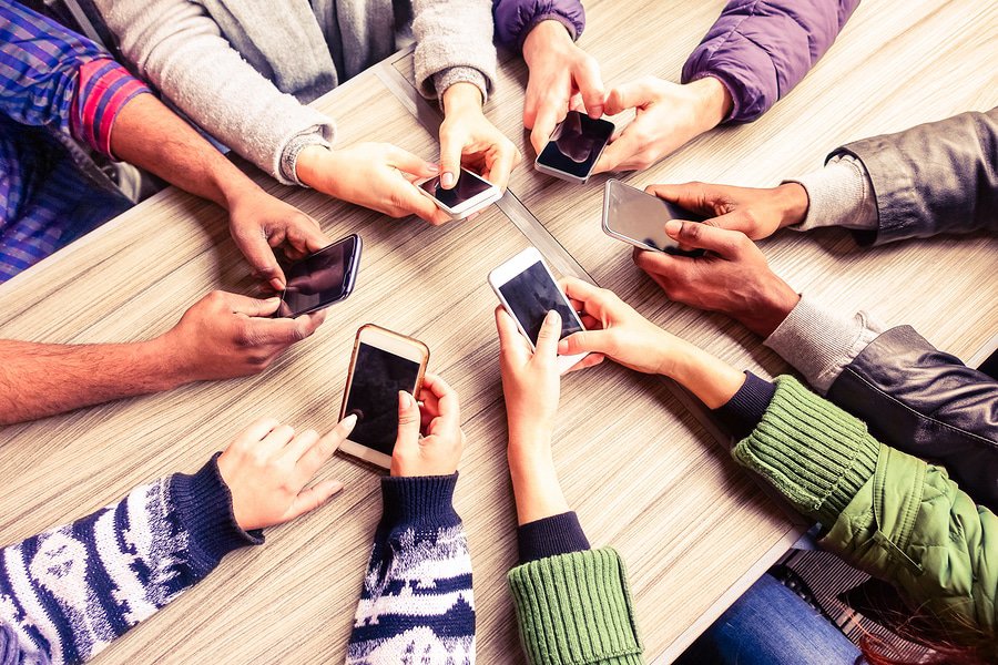 A photo of six people sitting at a table engrossed in their smartphones.