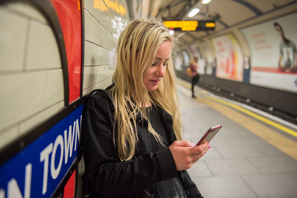 A photo of a woman waiting for a subway train, checking notifications on her mobile phone.