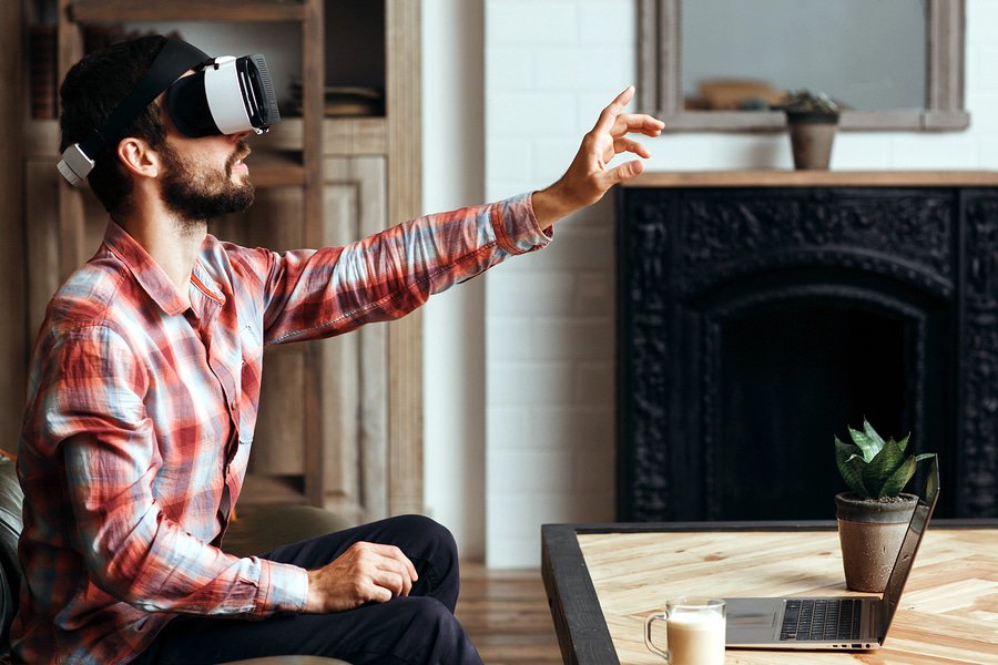 A photo of a man wearing a virtual reality headset and reaching out to touch something in front of him.