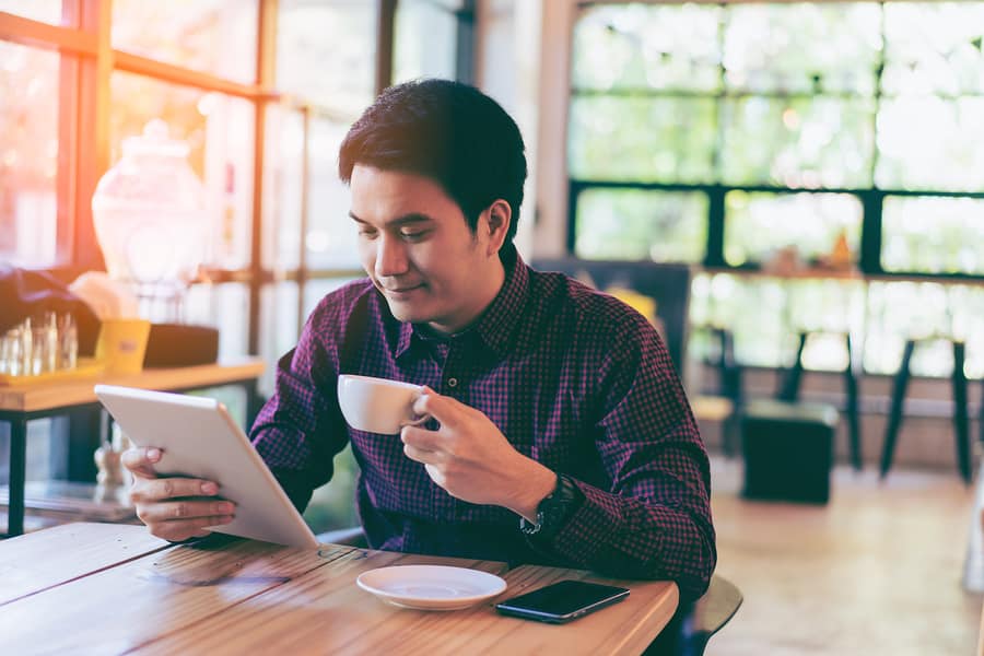 A photo of a man working on his tablet at a coffee house at sunset.