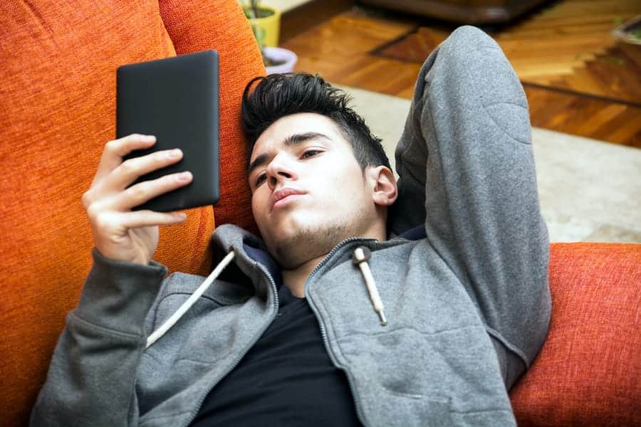 A photo of a man lying on a couch, reading a book on an e-reader.