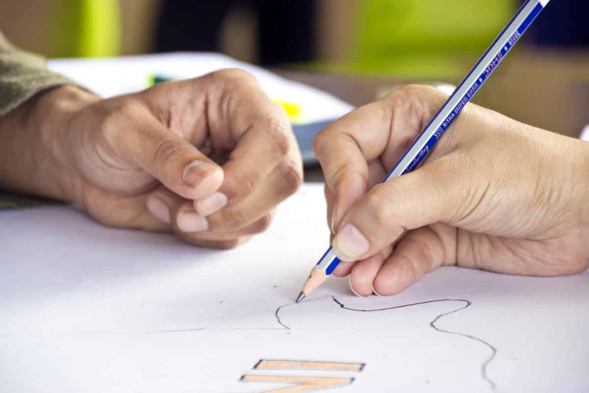 A photo of two hands from different people working on a sketch together.