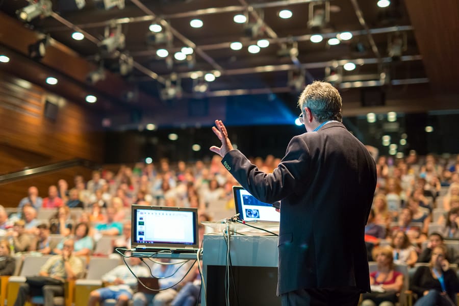 A photo of a man giving a presentation to a large group of people.