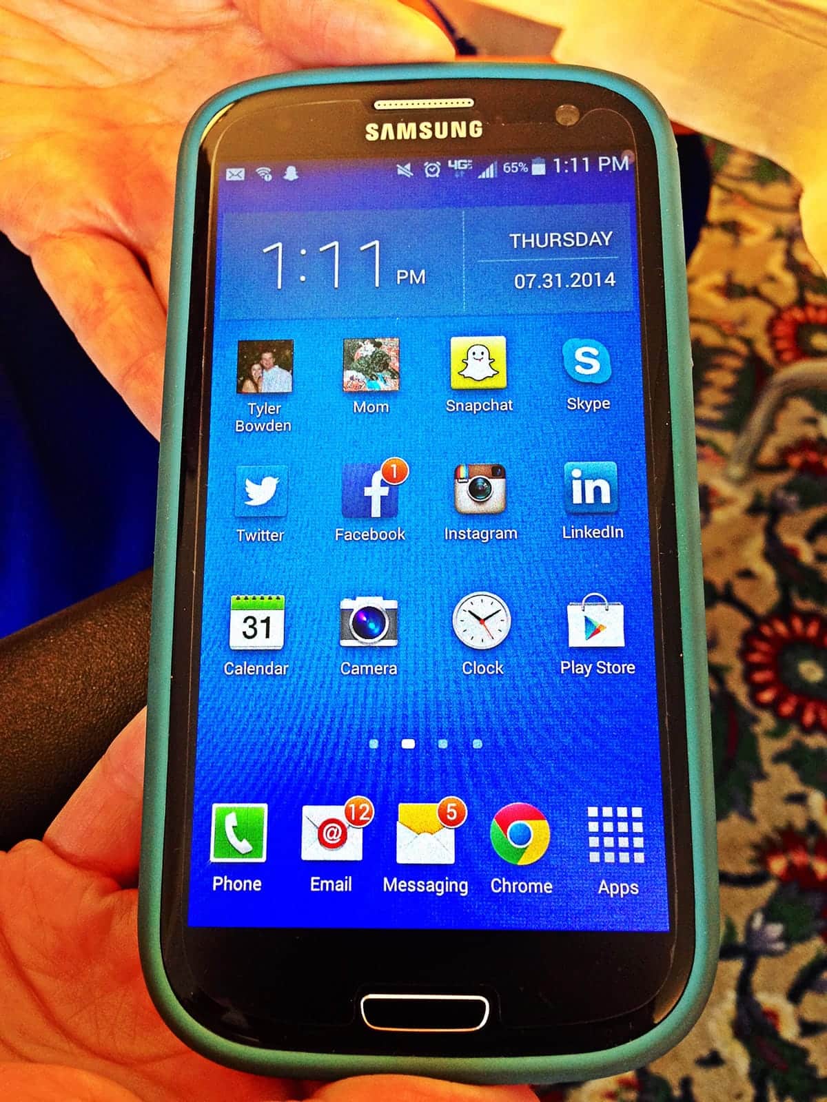A photo of a person holding a Samsung smartphone displaying the home screen.