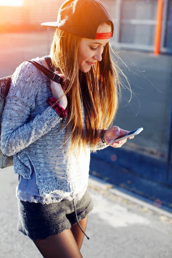 A photo of a young woman walking down the street, looking at her smartphone.