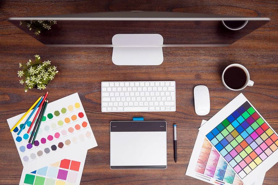 A photo of a designer’s desk, complete with color charts, a computer, and a drawing tablet.