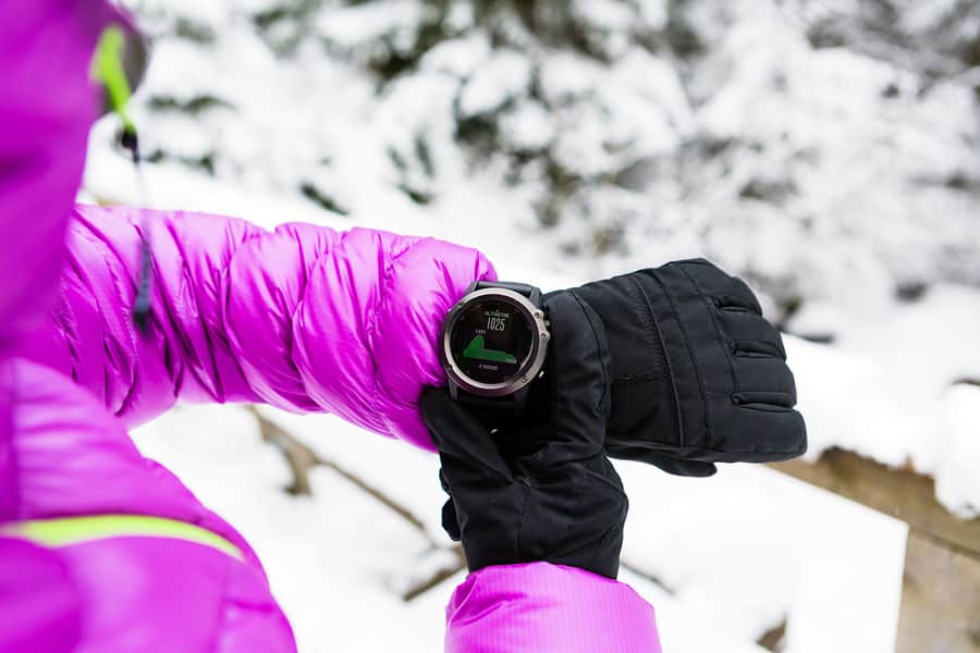 A photo of a woman checking the elevation on her smartwatch during a snowy hike.