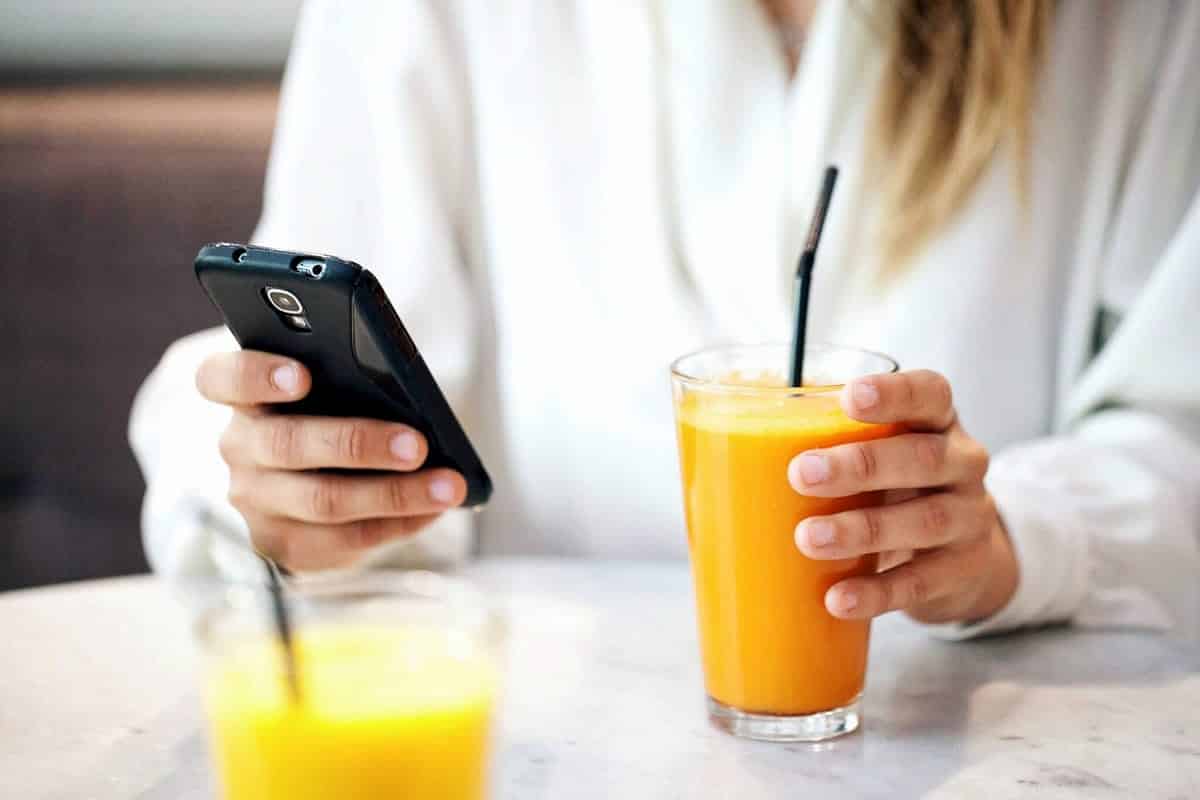 A photo of a woman checking her smartphone over a morning smoothie.