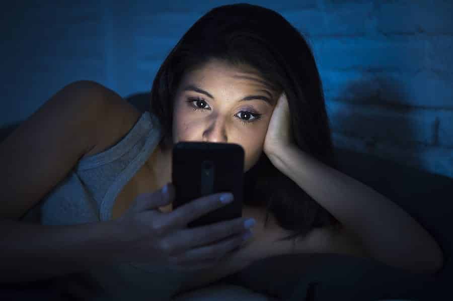 A photo of a woman lying in bed late at night, engrossed in her smartphone.