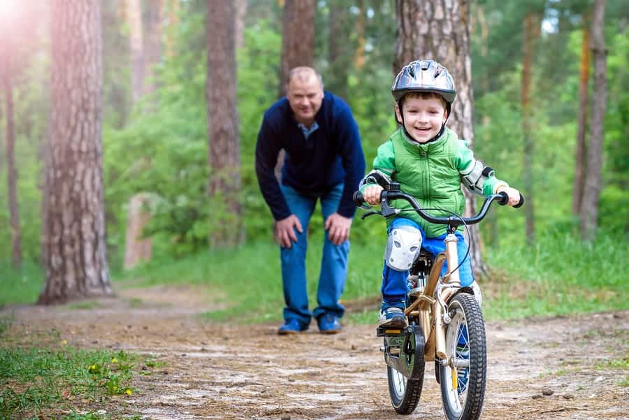 A photo of a dad helping his child learn how to ride a bike without training wheels.