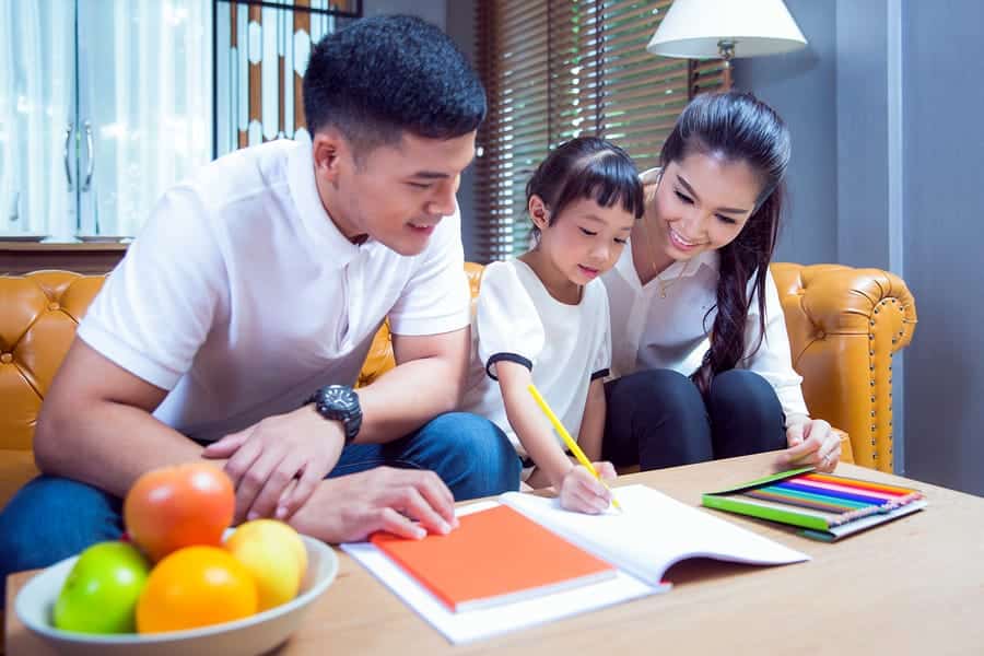 A photo of a mom and dad helping their daughter with her homework.