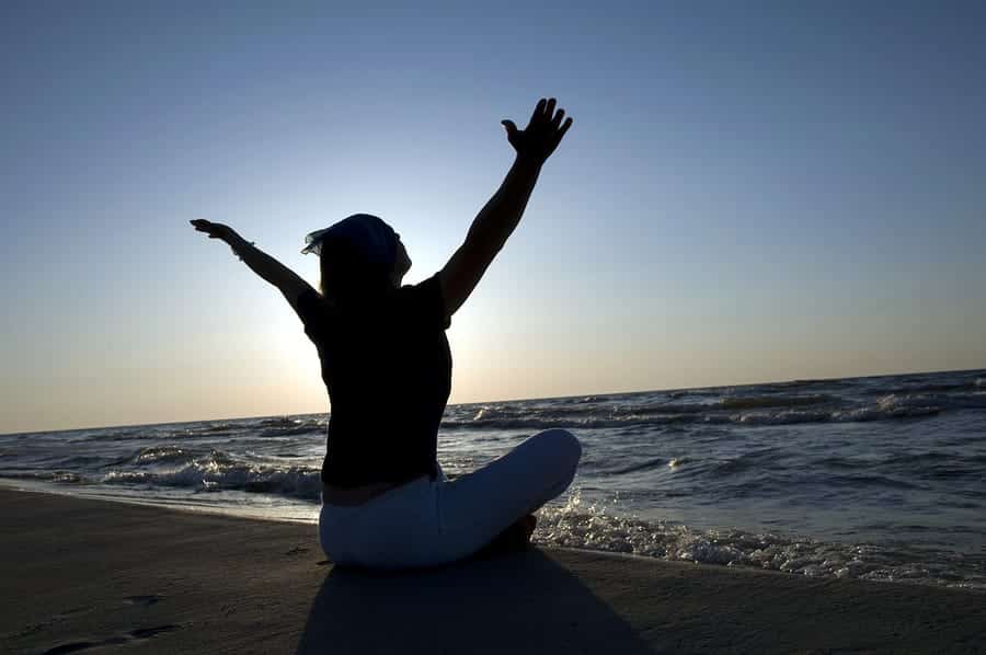 A photo of a woman meditating on a beach at sunrise.