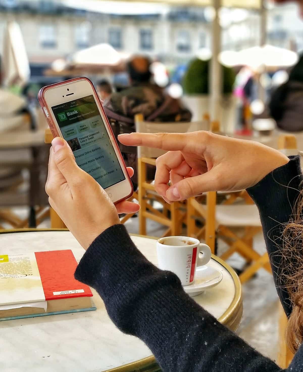 A photo of a person doing some online banking through a mobile app while sitting at an outdoor cafe.