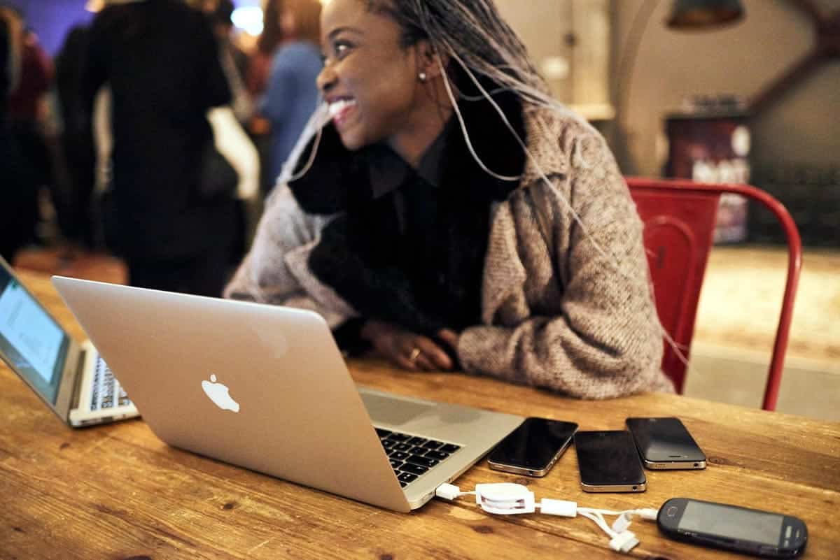A photo of a happy woman surrounded by laptops and various smartphones.