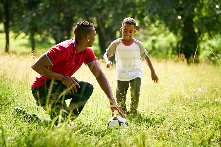 A photo of a dad helping his son learn how to play soccer.