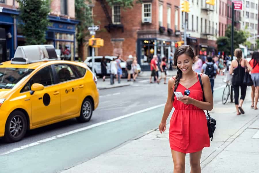 A photo of a woman looking at her phone as she walks down a busy city street.