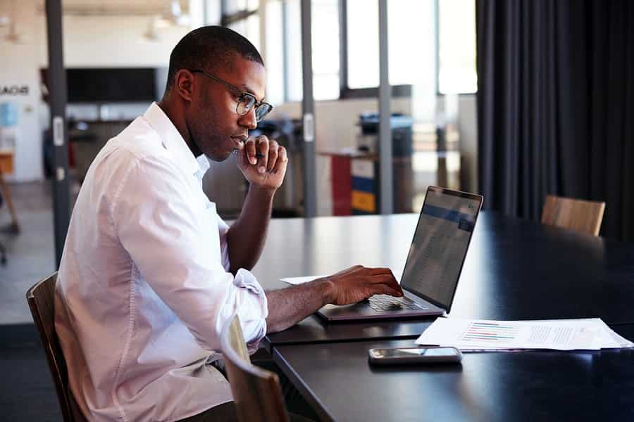 A photo of a man working on a laptop in a sunlit modern office.