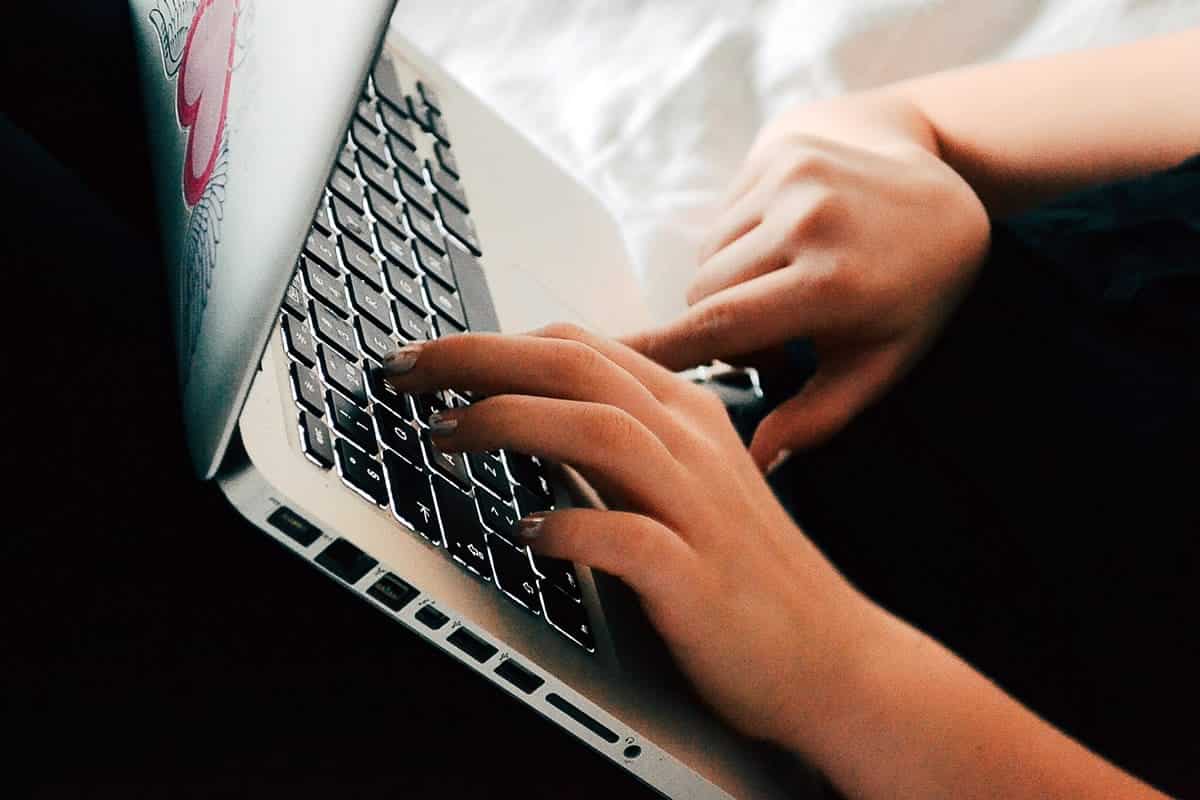 A photo of a person working on their laptop in a reclined position on a couch.