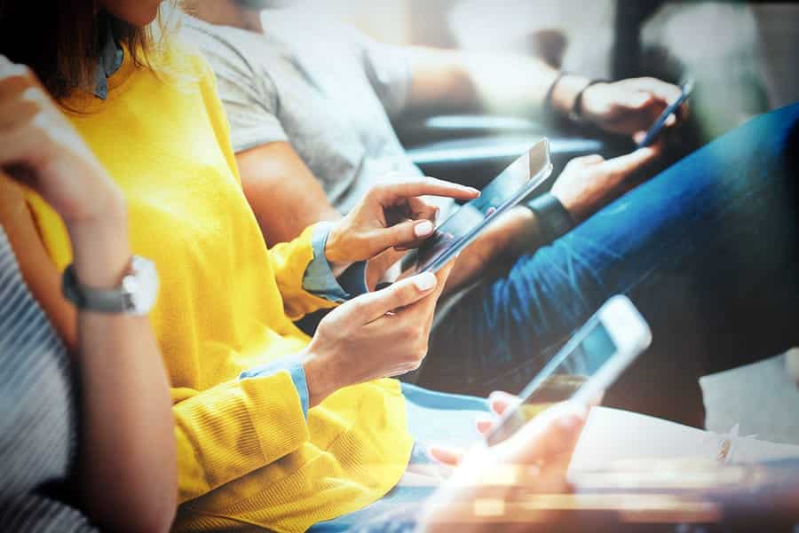 A photo of three friends sitting side by side, each reading something on their own smartphone.