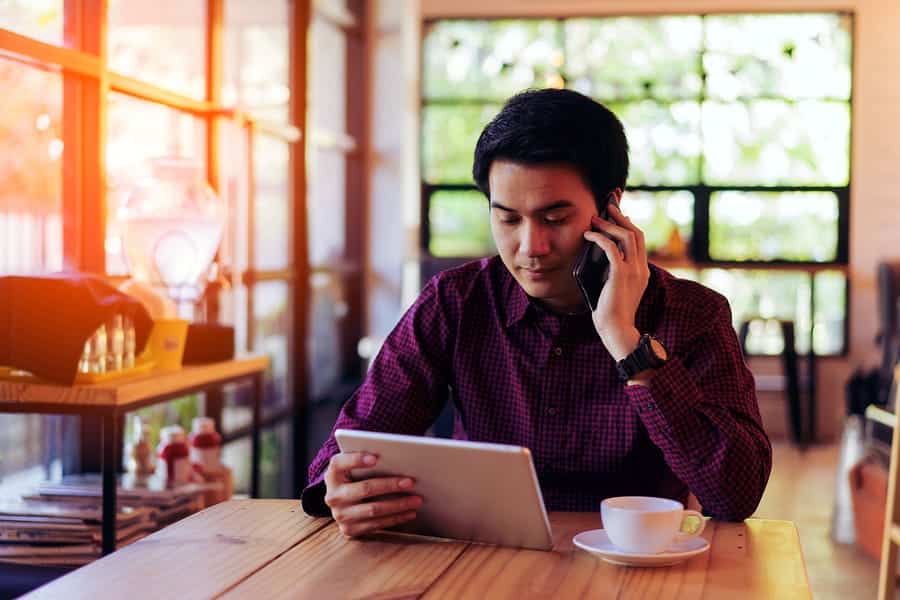 A man works while on his phone at a coffee shop.