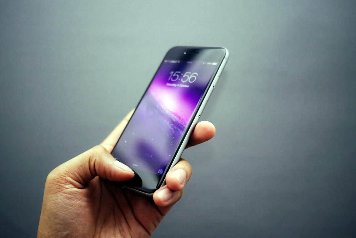 A photo of a person holding an iPhone with a purple background.