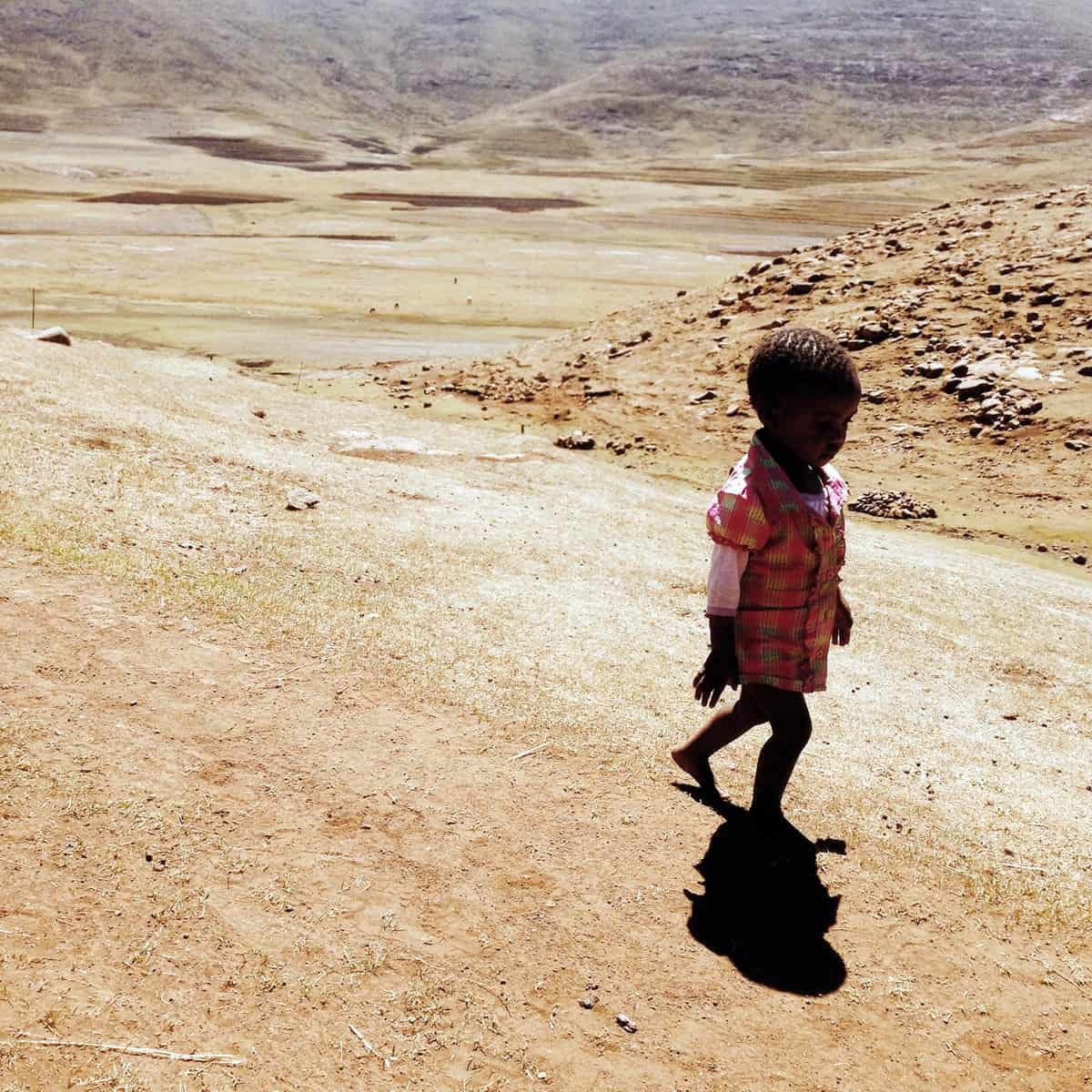 A photo of a child walking barefoot on a dirt road.