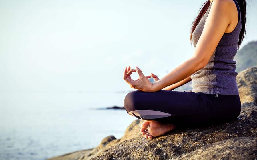 A photo of a woman meditating on a cliff by the ocean.