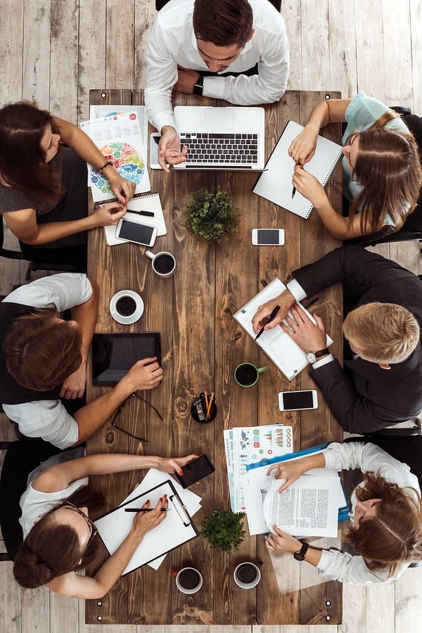 A top-down view of a development team sitting around a wood table for a meeting.