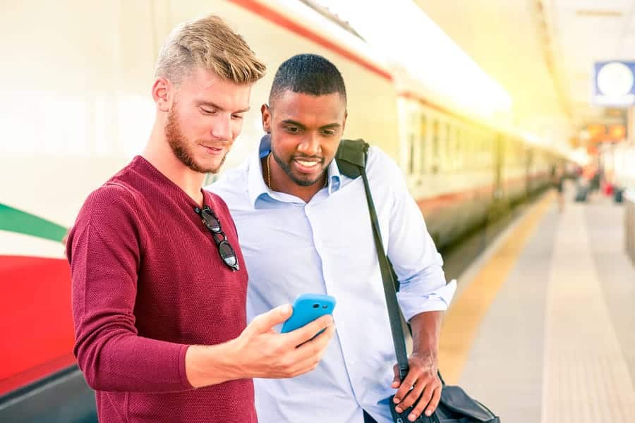 A photo of two men looking at a smartphone screen while waiting for a commuter train.