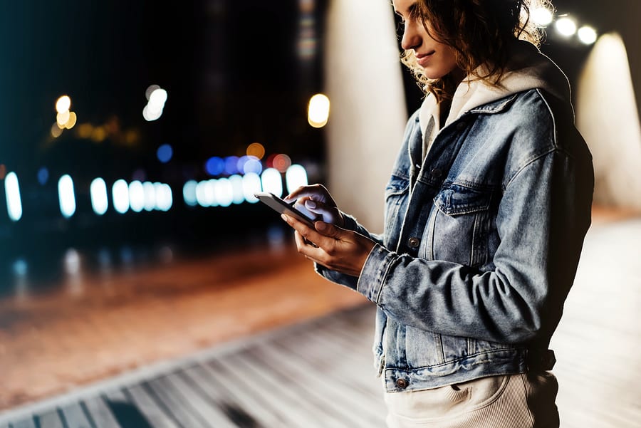 A photo of a woman checking her smartphone at night on the boardwalk.