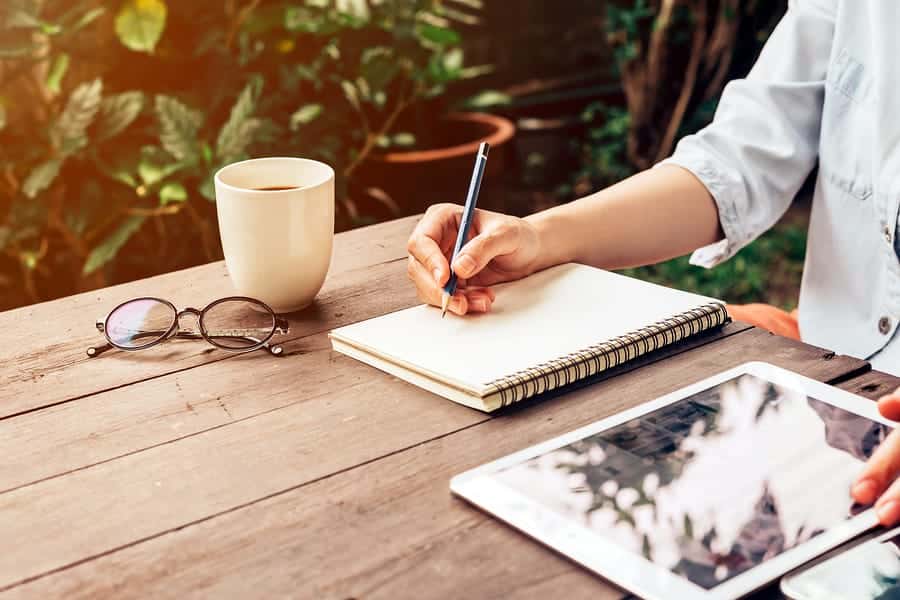 A photo of a designer sketching in a notebook outside with morning coffee.