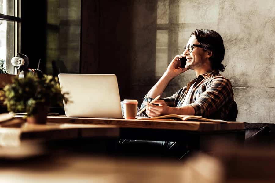 A photo of a man smiling and talking on a cell phone at his desk.