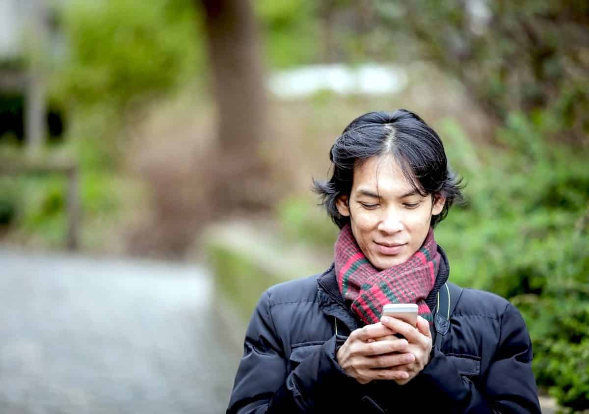 A photo of a man walking on a trail while checking his smartphone.