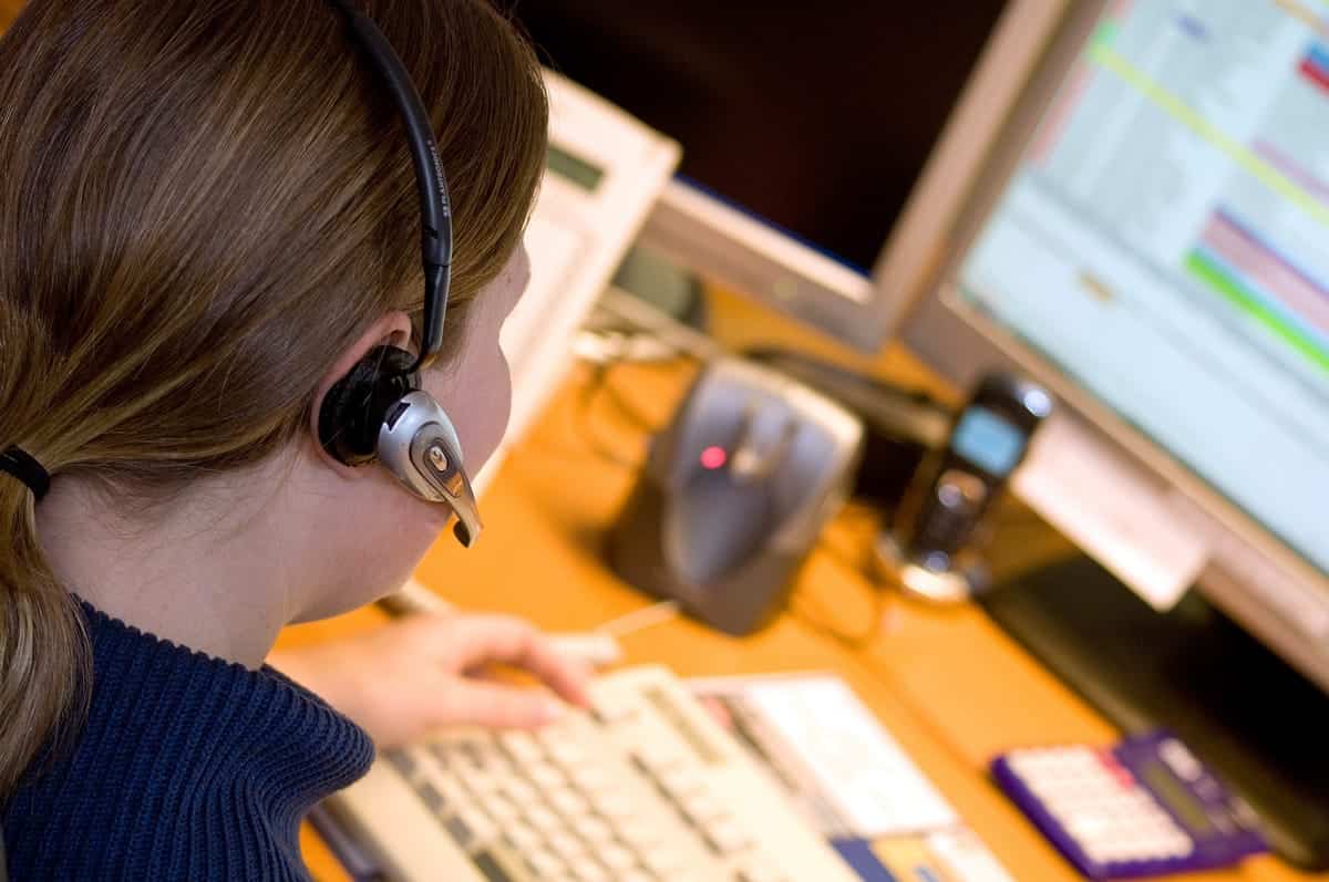 A photo of a woman using a headset to talk to a customer on the phone.