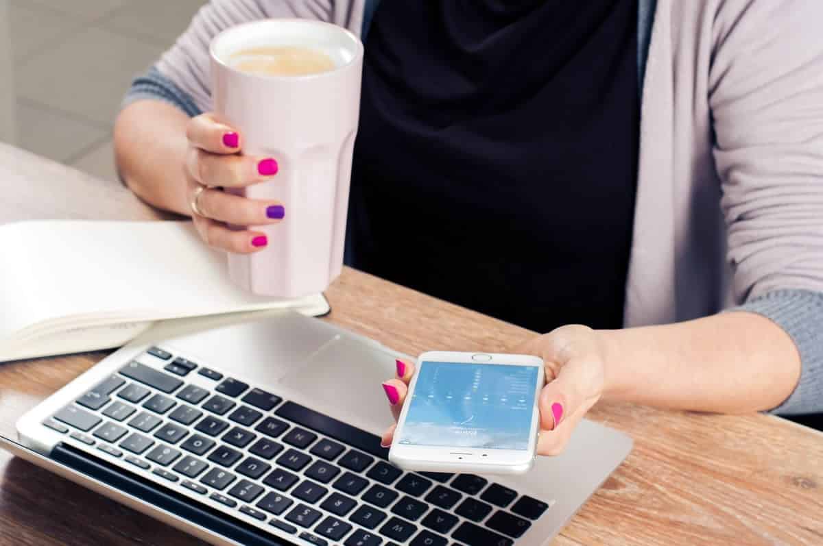 An image of a woman holding her phone and a coffee drink.