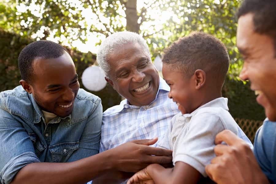 A photo of a grandfather laughing with his sons and grandson at a family gathering.